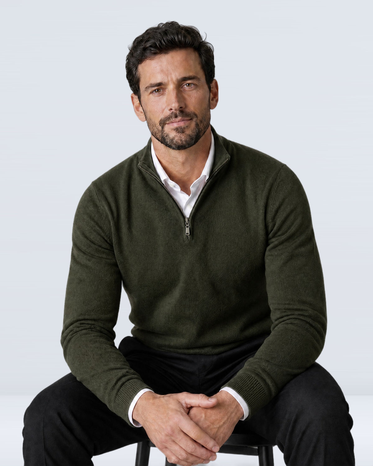 Hombre sentado con suéter WINDSOR verde oliva y pantalón de vestir negro